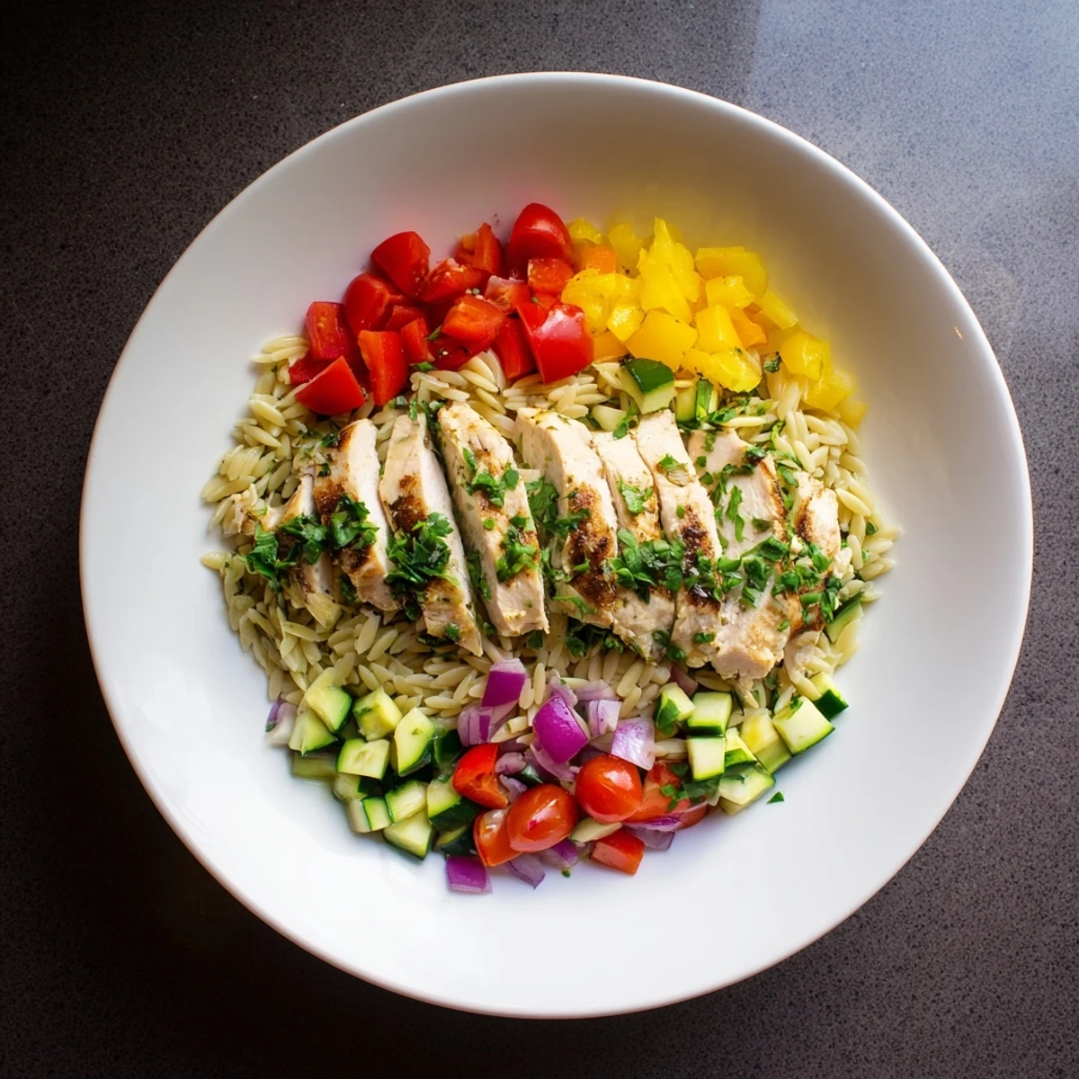 Golden brown glazed chicken resting atop a bed of orzo mixed with zucchini bell peppers and cherry tomatoes