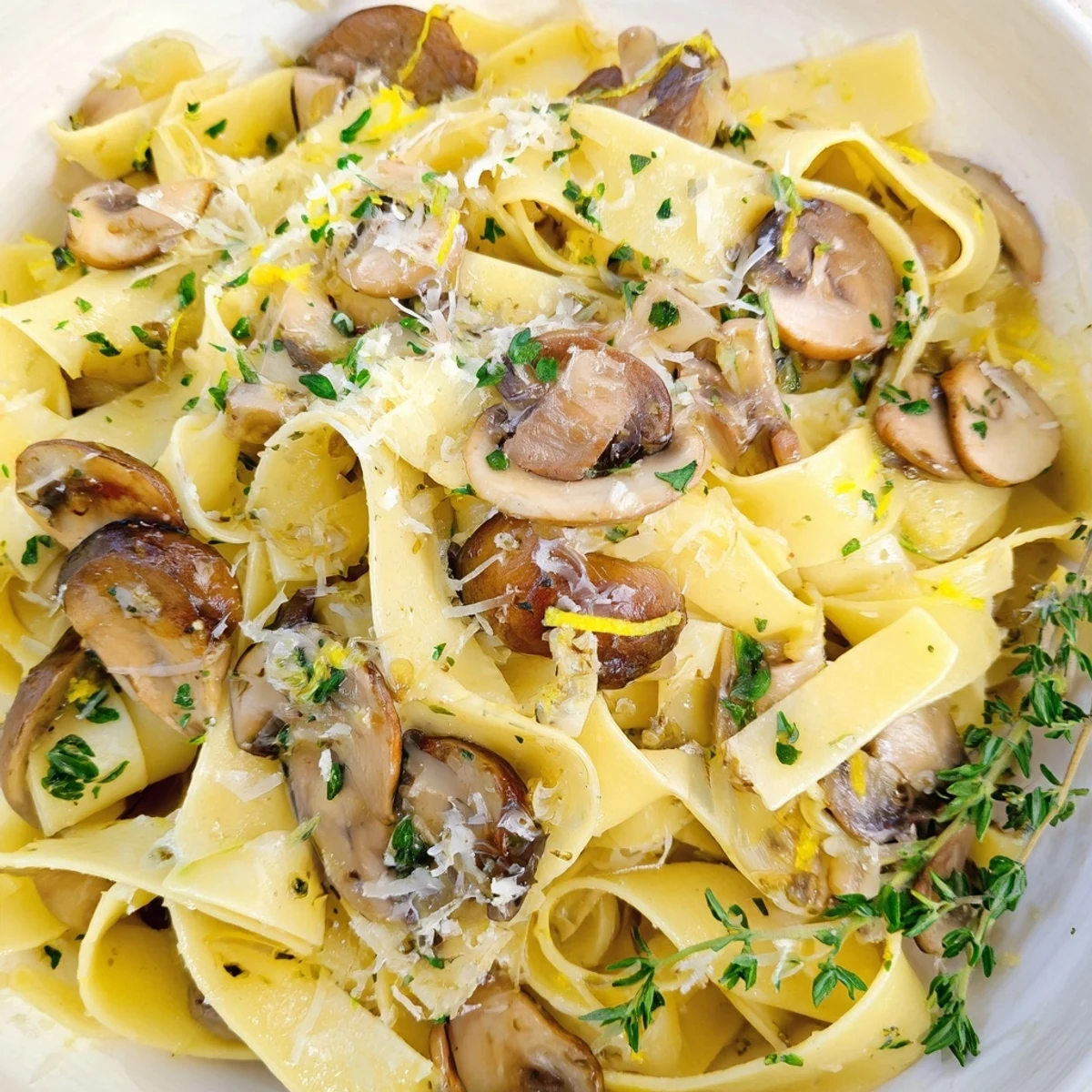 Twirled pappardelle pasta topped with garlicky sautéed mushrooms and grated Parmesan cheese on a white plate
