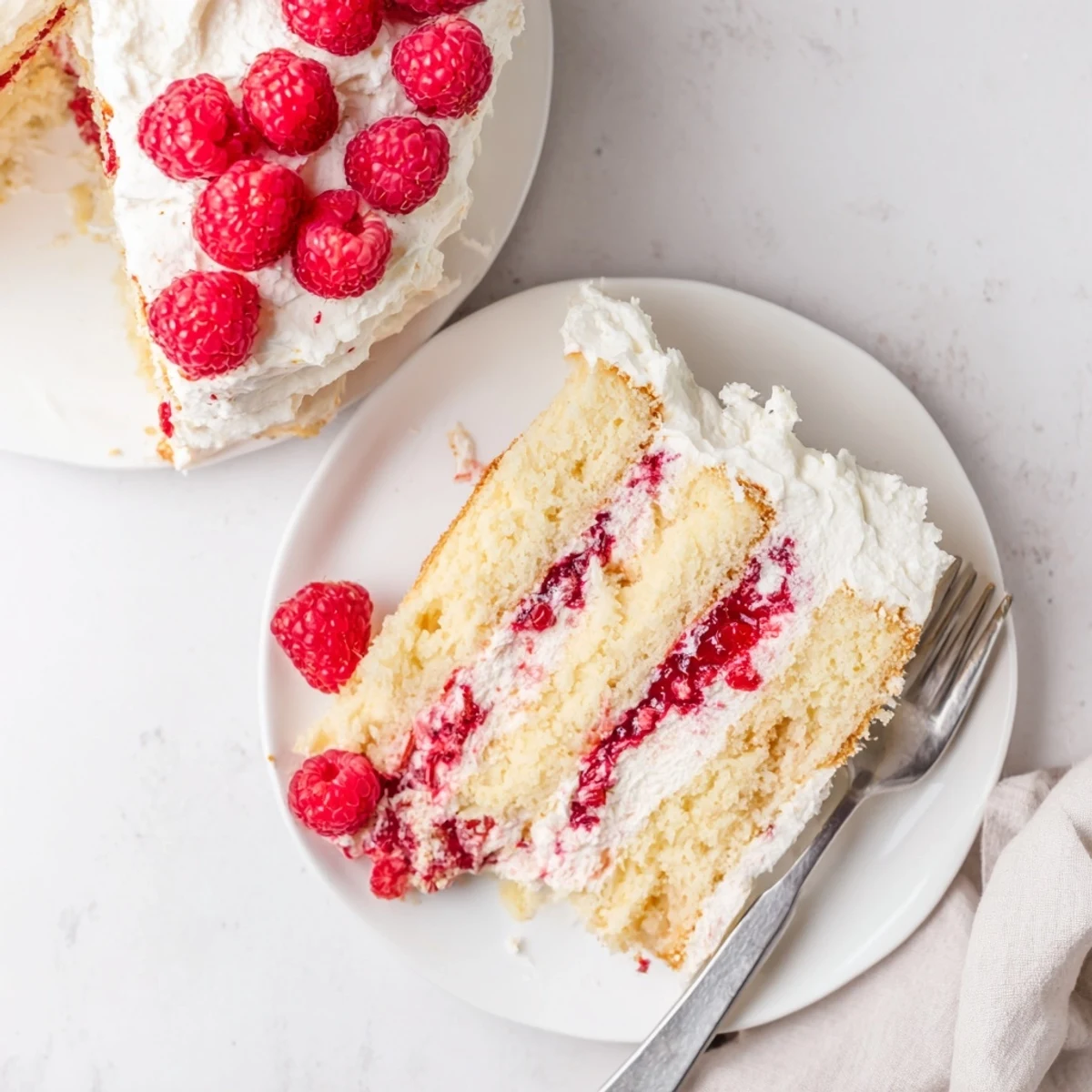 Elegant white chocolate raspberry cream cake with whipped cream frosting and whole raspberries on top