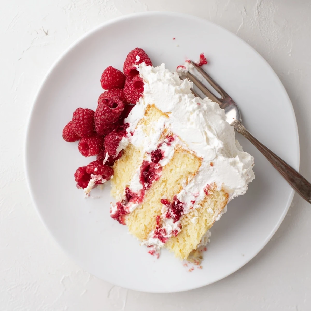 Slice of white chocolate raspberry cream cake on a white plate topped with fresh berries