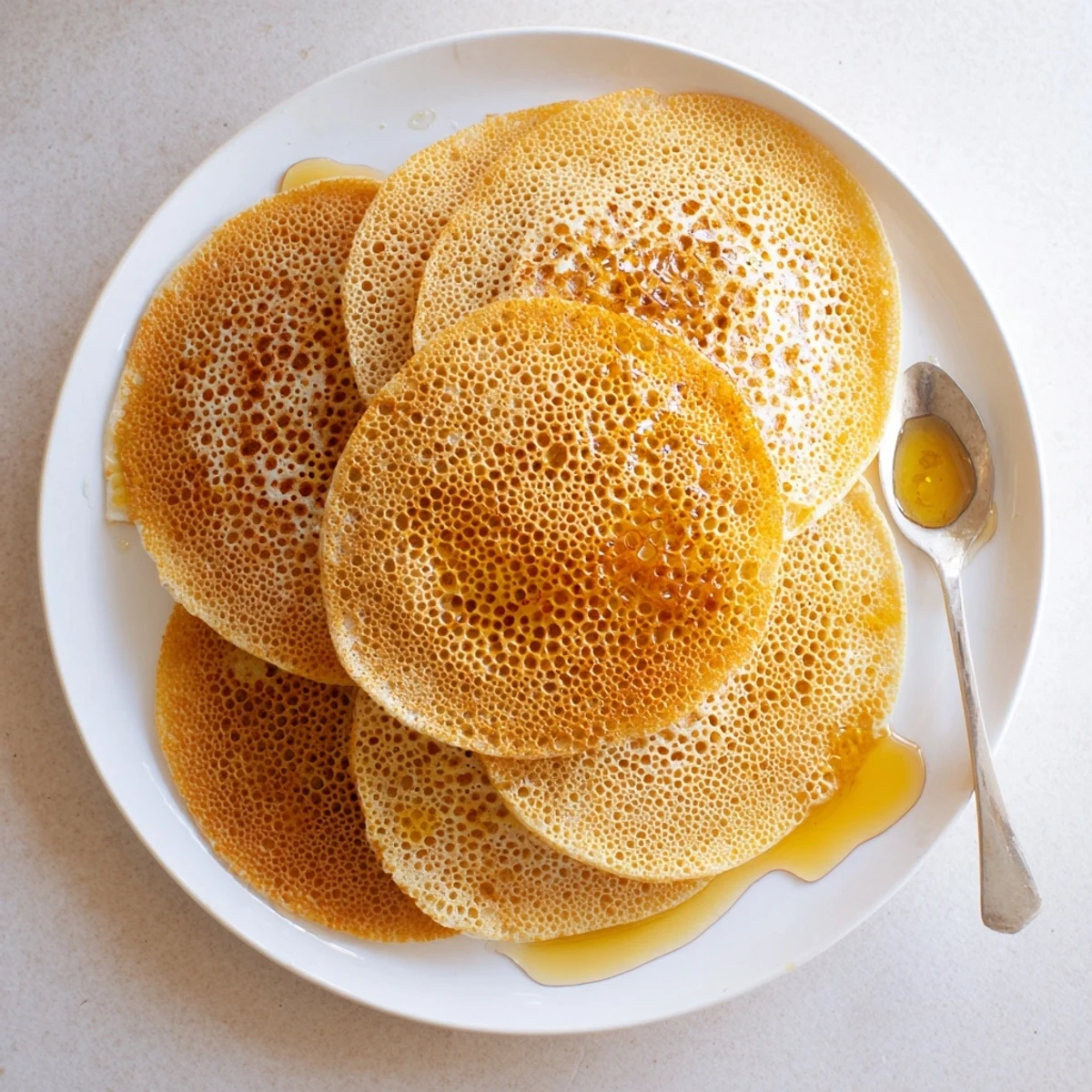 Golden Moroccan baghrir pancakes featuring signature honeycomb bubbles drizzled with melted butter and sweet honey