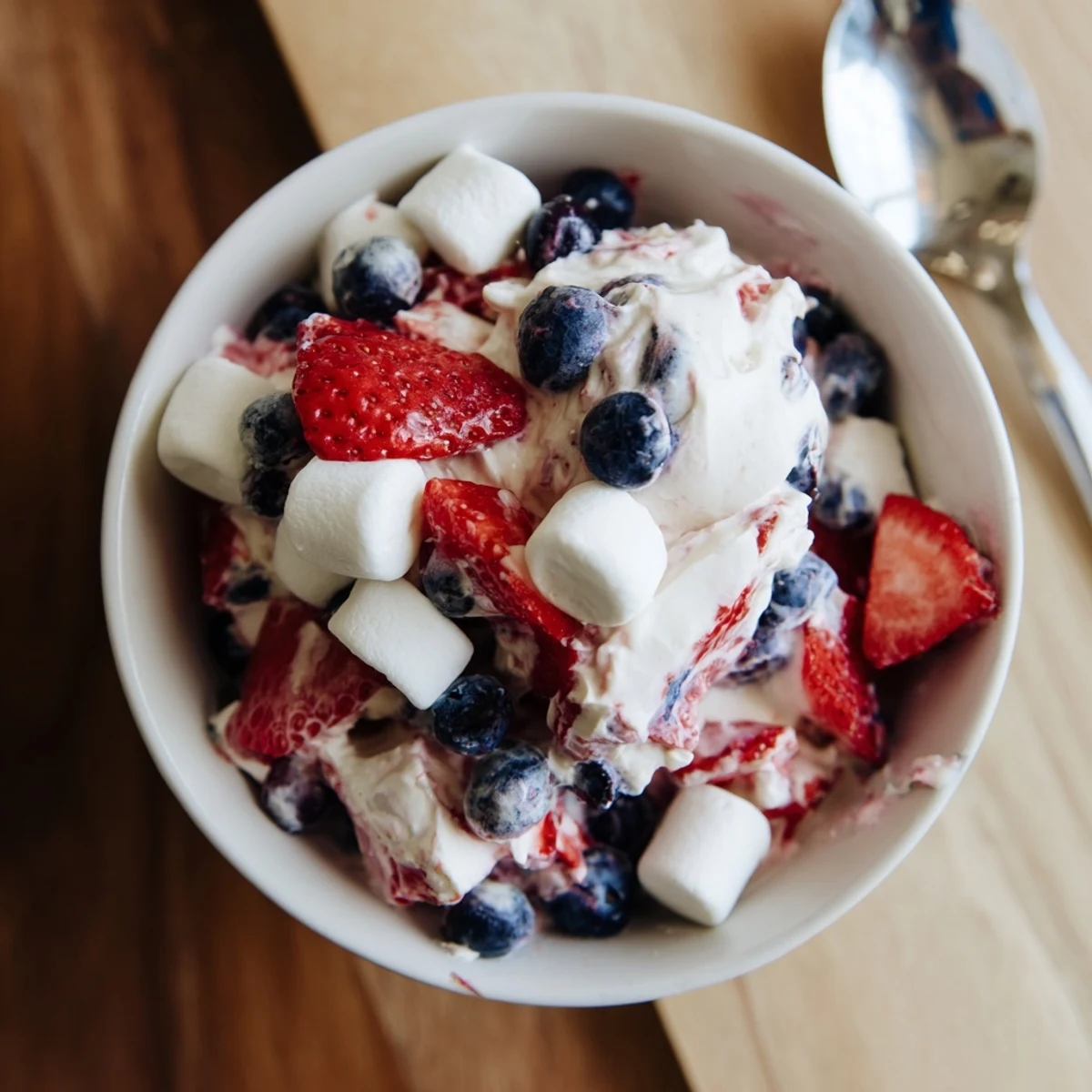 Creamy red white blue cheesecake salad loaded with fresh berries and marshmallows in a glass bowl
