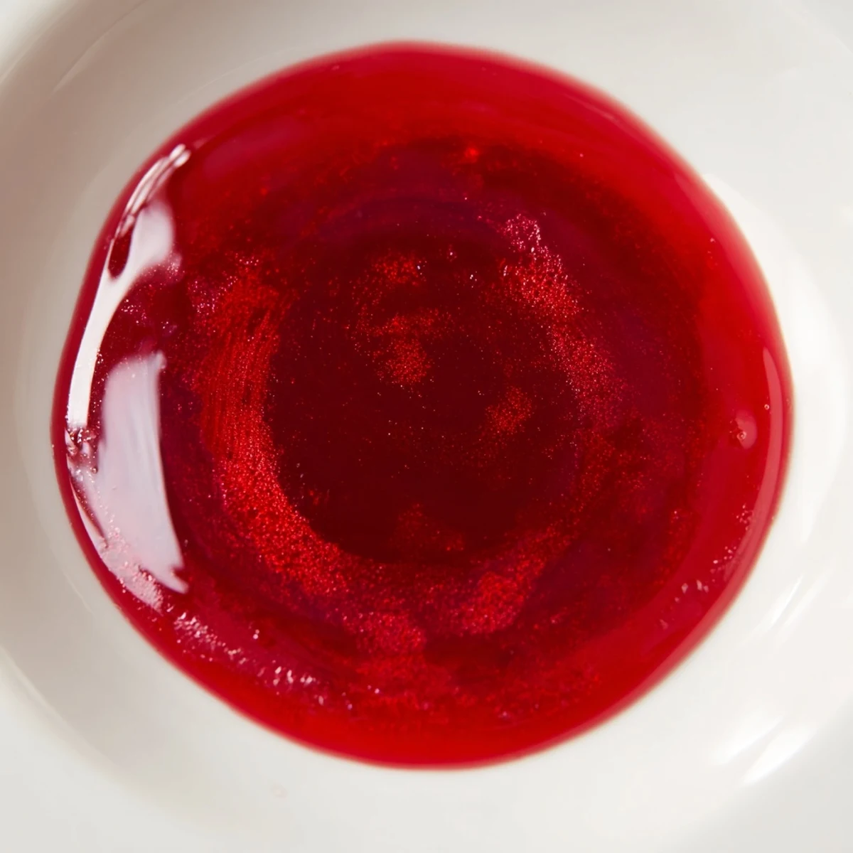Glass jar of vibrant homemade cranberry syrup catching light with wooden spoon nearby