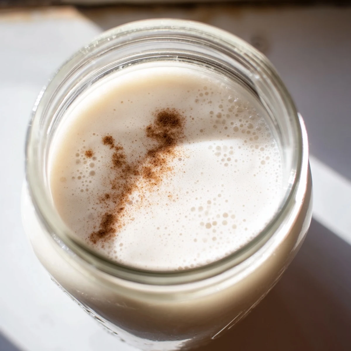 Fresh almond milk being poured from a blender into a clear glass container