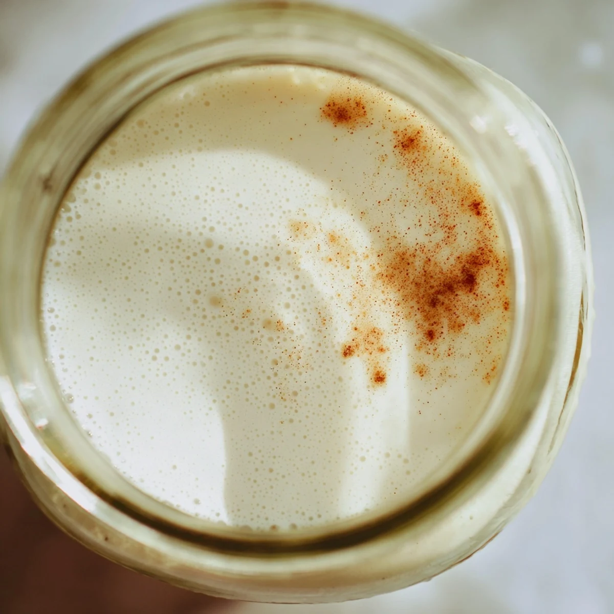 Glass jar filled with creamy white homemade almond milk on a wooden kitchen counter