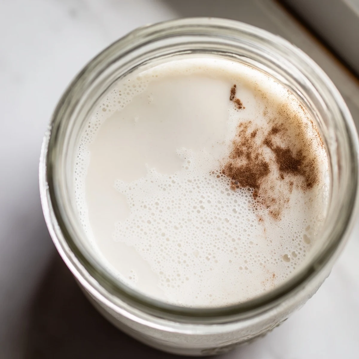 Frothy homemade almond milk in a mason jar with almonds scattered nearby