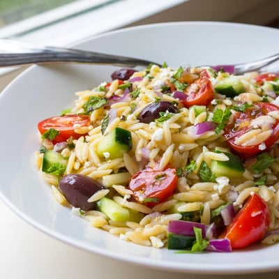 Mediterranean orzo pasta salad tossed with cucumbers, olives, and fresh herbs